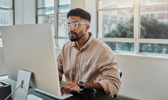 man sitting at desk working on desktop computer