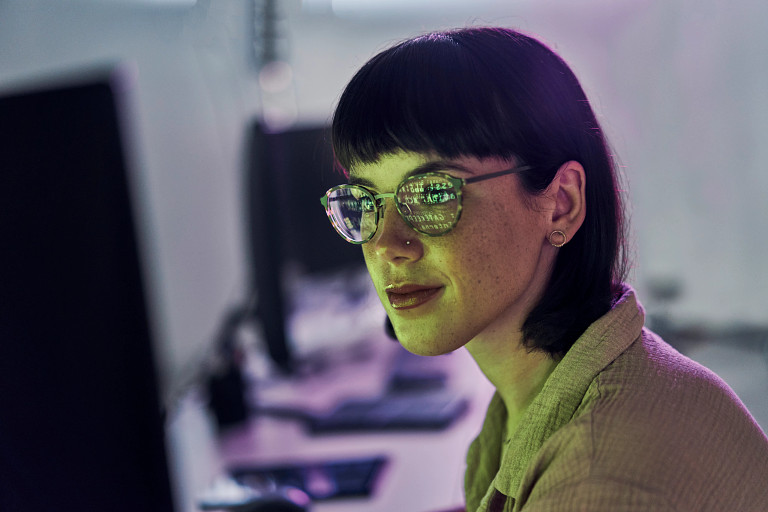 woman looking into screen with computer data reflected in her glasses