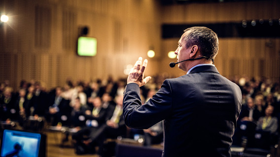 A man with a microphone standing on stage presenting at a corporate event